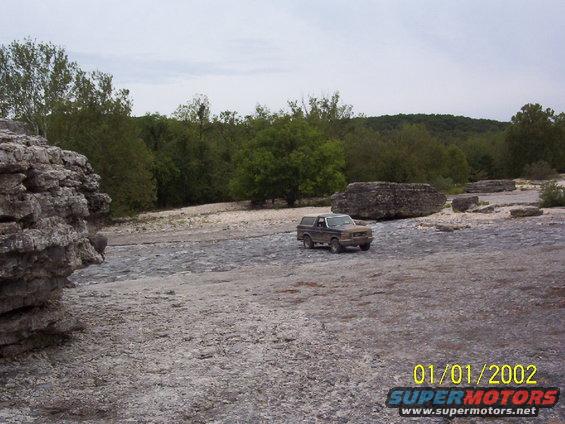 Brown Ford Bronco parked on rocky terrain with trees in the background