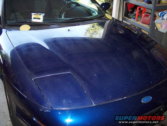 Blue car hood with pop-up headlights, a yellow sponge, and a cleaning product on the windshield