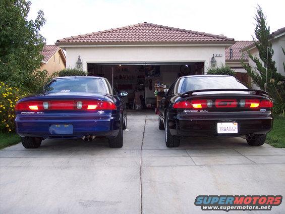 Two 1995 Ford Probes parked in a driveway in front of a garage, one blue and one black