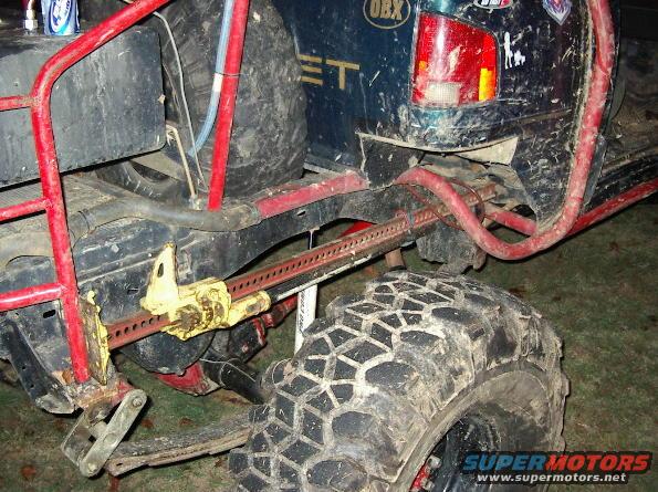 Off-road vehicle rear axle with hi-lift jack attached to frame, large mud tire visible