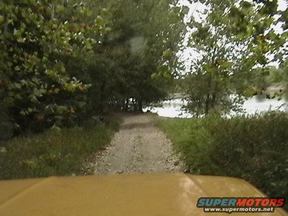 Yellow vehicle hood on dirt road leading to water and trees