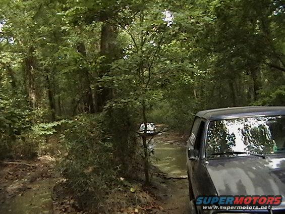 Dark SUV on muddy forest road, 1986 Ford Bronco