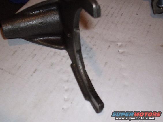 Dark metal part with a hook and a lever arm, resting on a white surface