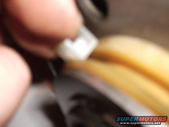 Hand holding a white plastic clip near a yellow component