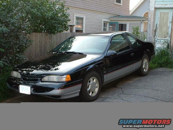 1995 Ford Thunderbird coupe parked on asphalt next to a wooden fence and house