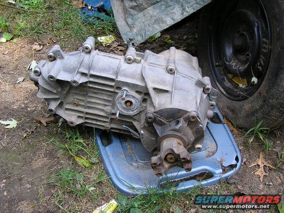 Aluminum transfer case with a U-joint flange, resting on a blue plastic tray outdoors