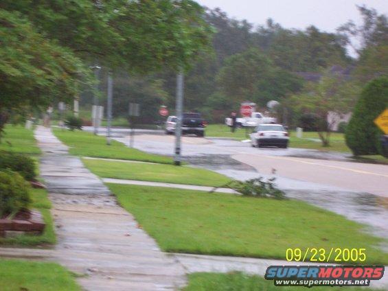 Street with sidewalk, grass, trees, and cars driving on a wet road. Date stamp reads 09/23/2005