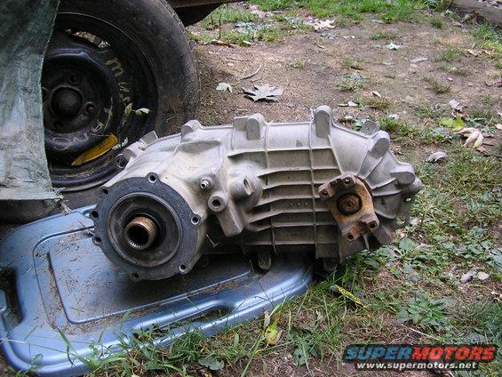 Aluminum transfer case with a U-joint flange, resting on a blue plastic tray next to a tire