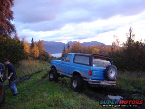 Blue 1988 Ford Bronco on muddy trail with mountains in background