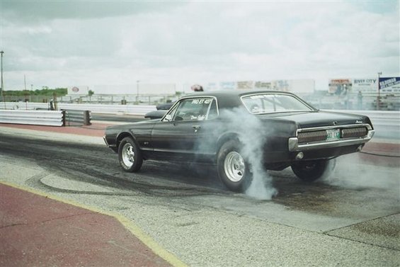 Black 1969 Mercury Cougar doing a burnout on a drag strip, smoke billowing from rear tires