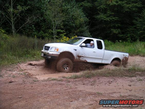 White pickup truck with lifted suspension driving through a mud pit