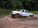 1994 Ford Bronco - A white pickup truck navigates a muddy trail, kicking up dirt as it goes.