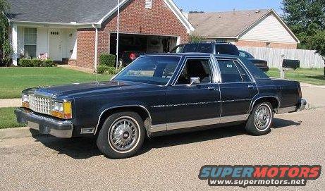 Dark blue sedan parked on street in front of a house. Another vehicle is in the driveway