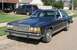 1985 Ford Crown Victoria LTD - A dark blue sedan is parked on the street in front of a house with a garage and a minivan.