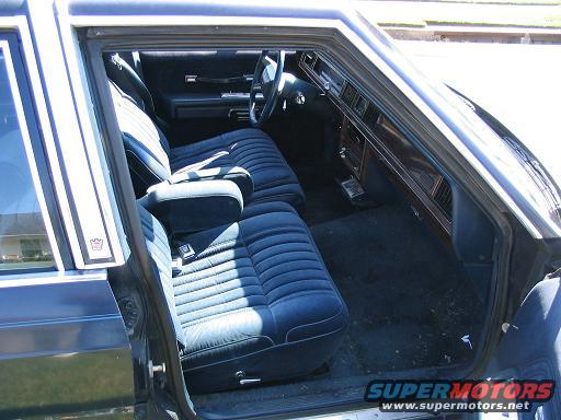 Blue velour interior of a dark blue sedan, showing front and rear seats, dashboard, and door panel. A small crown emblem is visible on the door pillar