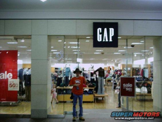 Man in orange shirt and cowboy hat stands in front of a Gap store