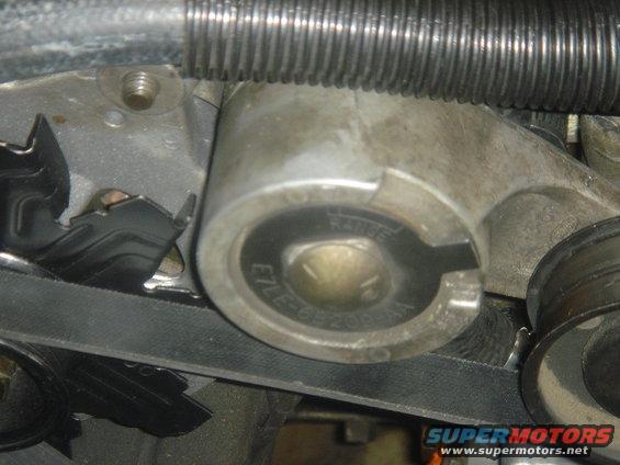 Close-up of an engine belt tensioner with part number E7LE-6B209-AA visible