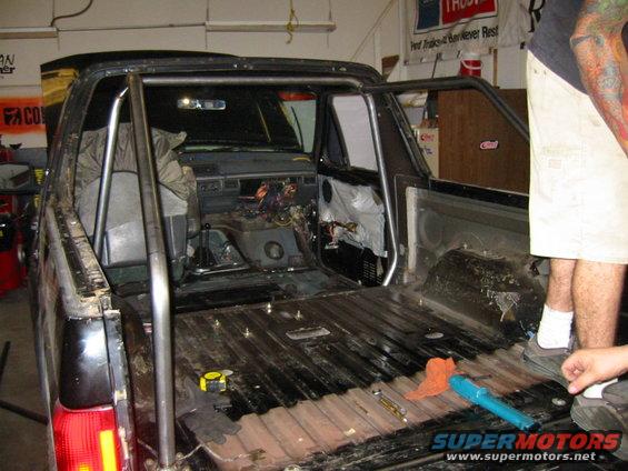 Pickup truck interior with roll cage, removed seats, and exposed wiring
