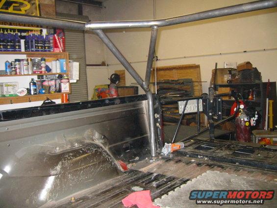 Rollcage tubing installed in a dirty truck bed with shelves of bottles in the background