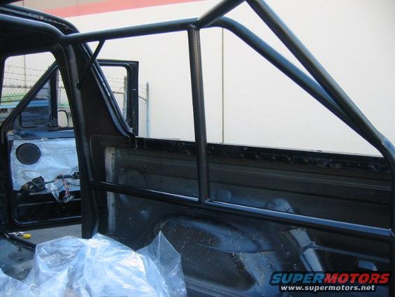 Interior view of a vehicle with a black roll cage installed. Door is open, showing interior panels and wiring