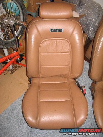 Tan leather car seat with a black emblem above the seat back