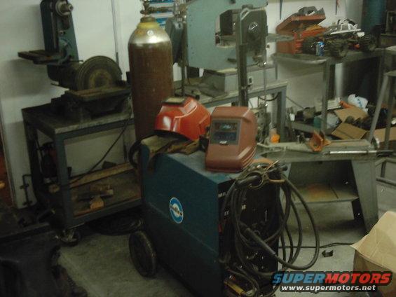 Miller welding machine with two welding helmets, gas cylinder, and various workshop tools