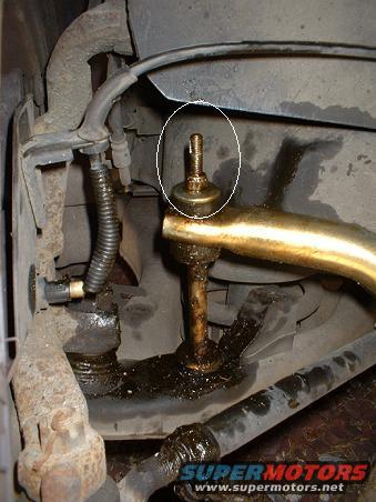 Close-up of a greasy suspension part with a bolt and nut, circled in white