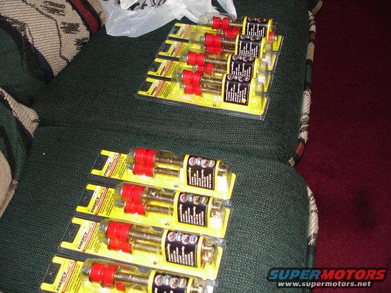 Several packages of red and gold suspension bushings are laid out on a green couch