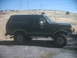 1987 Ford Bronco - This black Ford Bronco is shown from the side, parked on a gravel surface with a dry, hilly landscape behind it.