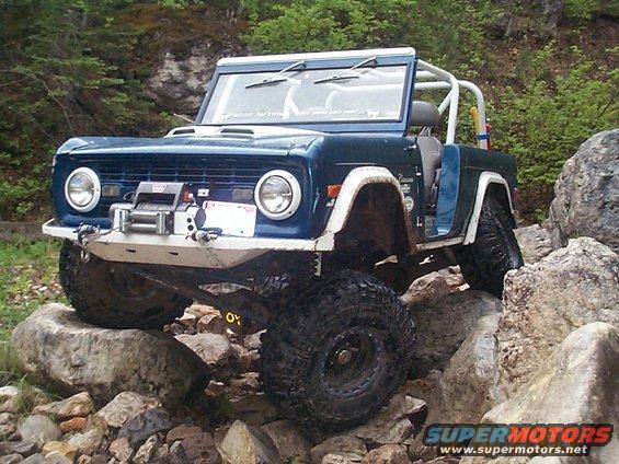Blue off-road SUV with a winch and roll cage navigating rocky terrain