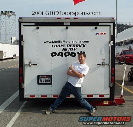 Man in front of white trailer with text, red truck in background