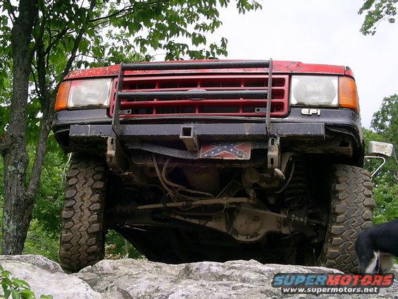 Front view of a red SUV with a brush guard and large tires, parked on rocks