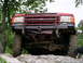 1985 Ford Bronco - The front of a red SUV is shown with a brush guard and off-road tires, positioned on a rocky surface.