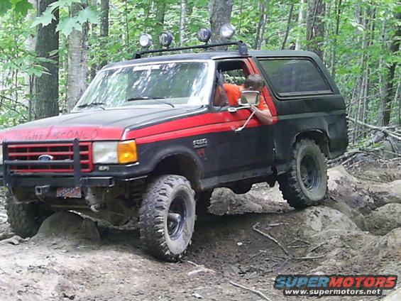 Black and red 1985 Ford Bronco climbing rocks off-road