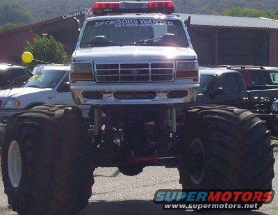 1995 Ford Bronco monster truck with large tires and light bar, "SPONSORS WANTED" text on windshield