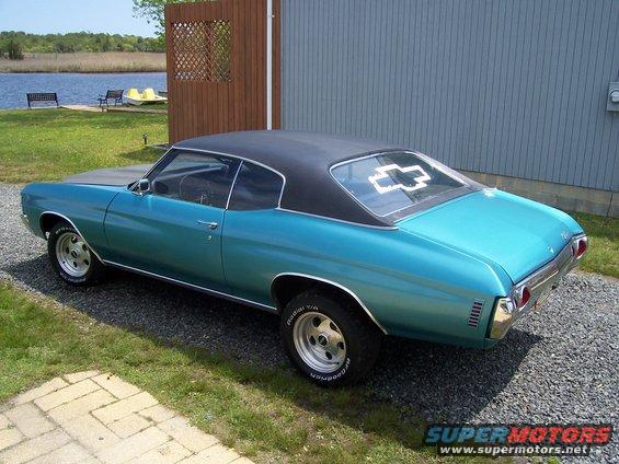 1971 Chevrolet Chevelle coupe, teal with black vinyl roof, parked on gravel near a building and water
