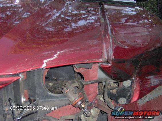 close-up of a damaged red car fender with exposed wiring and a light bulb socket
