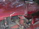 1996 Ford Mustang - The front fender of a red car shows damage and exposed components, including wiring and a light socket.