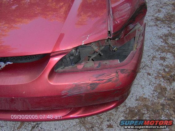 Front end of a red car with damage to the bumper and headlight area. Shows a 1996 Ford Mustang badge