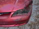 1996 Ford Mustang - The front of a red vehicle shows significant damage to the bumper and headlight assembly, with visible scrapes and scraped paint.