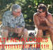 1997 Ford Crown Victoria - Two men are sitting on a bench outside, with red text and a website address superimposed on the photo.