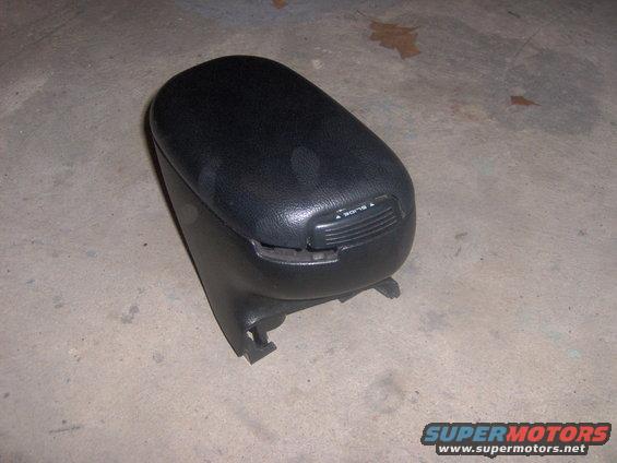 Black car armrest console with a slide lever on top. It's sitting on a concrete floor