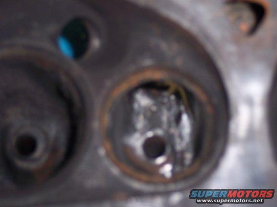Close-up of engine cylinder head with two openings, one showing damage