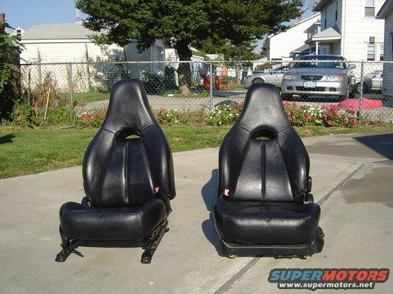 Two black leather car seats sitting on a concrete driveway
