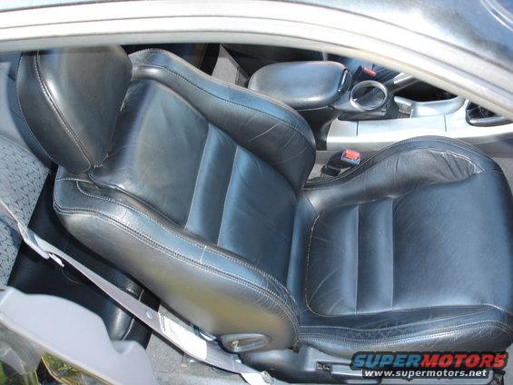 Black leather driver's seat with visible wear, seen from above and to the side. A seatbelt is visible