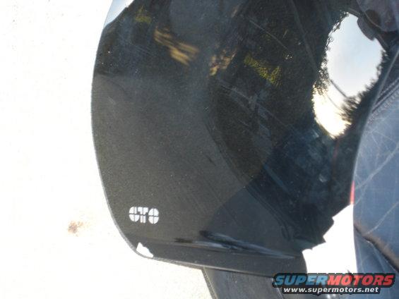 Close-up of a black car fender with a white 'GTO' emblem. Reflections show trees and sky
