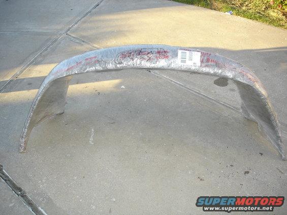 Car part wrapped in plastic with red lettering and a barcode label