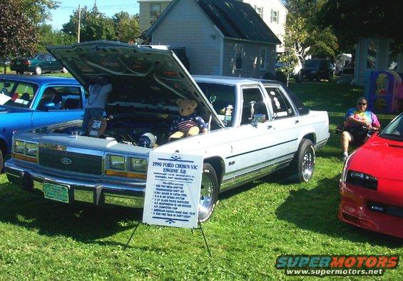 White 1990 Ford Crown Victoria with hood open, teddy bear inside, parked on grass