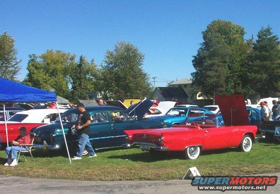Several classic cars parked on grass under a blue tent and in the open