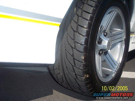 White car's front wheel and tire with a yellow stripe on the body